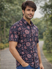 Man wearing a patterned jahota shirt standing outdoors with greenery in the background