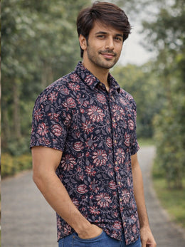 Man wearing a patterned jahota shirt standing outdoors with greenery in the background